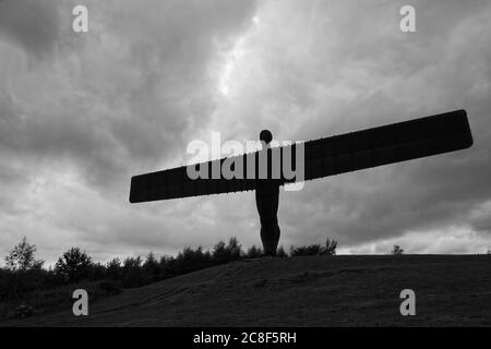 La statue emblématique en fer de l'Ange du Nord, conçue par Anthony Gormley, se dressant fièrement en silhouette contre un ciel bleu ciel rempli de nuages drastiques au soleil Banque D'Images