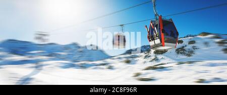 Télécabines sur les remontées mécaniques, dans le ciel bleu, au-dessus des montagnes enneigées de la station de ski des Alpes italiennes, le jour d'hiver ensoleillé Banque D'Images