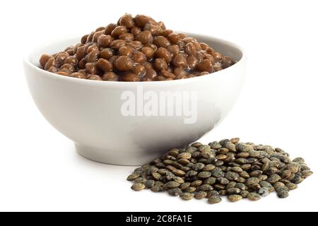 Lentilles vertes cuites du puy dans un bol en céramique blanc à côté de lentilles sèches isolées sur blanc. Angle bas. Banque D'Images