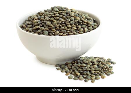 Lentilles vertes sèches du puy dans un bol en céramique blanc à côté d'une pile de lentilles isolées sur du blanc. Angle élevé. Banque D'Images