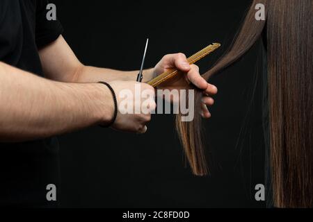 Coiffeur masculin avec peigne et ciseaux fait une coupe de cheveux pour une femme de gros plan Banque D'Images