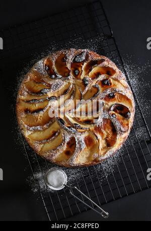 Tarte aux pommes cuite au four saupoudrée de sucre en poudre sur fond de bois noir. Banque D'Images