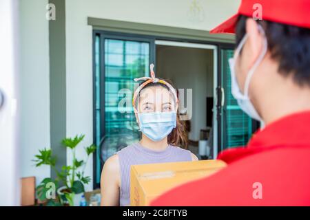 Les militaires de livraison asiatiques portent un uniforme rouge avec un capuchon rouge et un masque facial manipulant des boîtes en carton à donner à la cliente en face de la h Banque D'Images