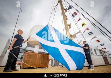 Rab McAulay (à gauche) et Tony Smith, de l'équipe d'entretien, lèvent le drapeau Saltyre sur le mât central du yacht royal Britannia pour marquer la réouverture de l'attraction touristique d'Édimbourg aux membres du public le lundi 27 juillet. Banque D'Images