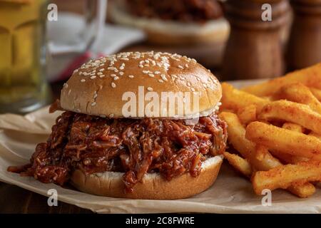 Griller un sandwich de porc tiré sur un pain de graines de sésame avec des frites Banque D'Images