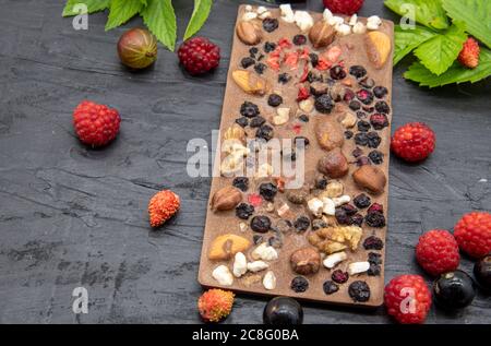 Des barres de chocolat, diverses baies mûres et des feuilles de menthe se trouvent sur un fond d'ardoise noire. Banque D'Images