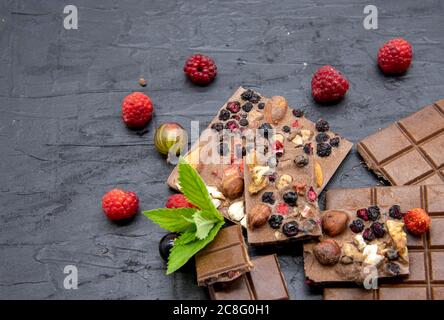 Des barres de chocolat, diverses baies mûres et des feuilles de menthe se trouvent sur un fond d'ardoise noire. Banque D'Images