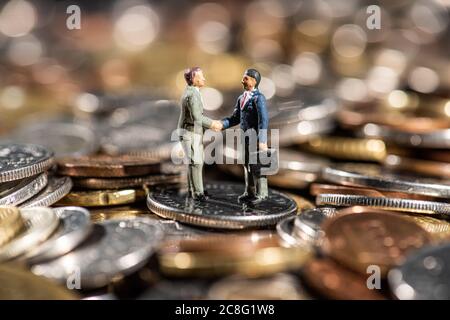 Petites figures de deux hommes qui se secouent la main sur un tas de pièces. Banque D'Images