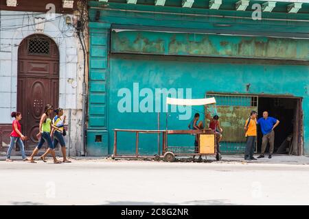 La Havane / Cuba - 04.15.2015: Trois femmes cubaines marchant devant un lieu de travail où deux hommes cubains sont debout et parlent, deux enfants jouant sur un ol Banque D'Images