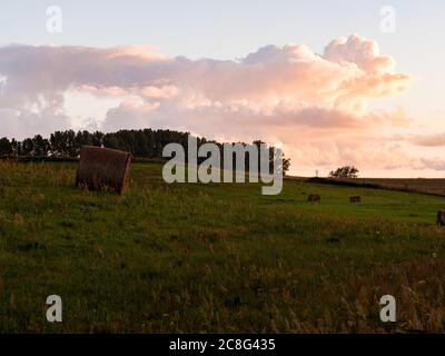 Sonnenuntergang Sonnenaufgang auf einem Getreidefeld auf der Insel Rügen mit einer Farm, Bäumen, Strohballen, roten Mohnblumen nach einem Gewitter Banque D'Images