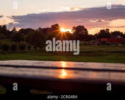 Sonnenuntergang Sonnenaufgang auf einem Getreidefeld auf der Insel Rügen mit einer Farm, Bäumen, Strohballen, roten Mohnblumen nach einem Gewitter Banque D'Images