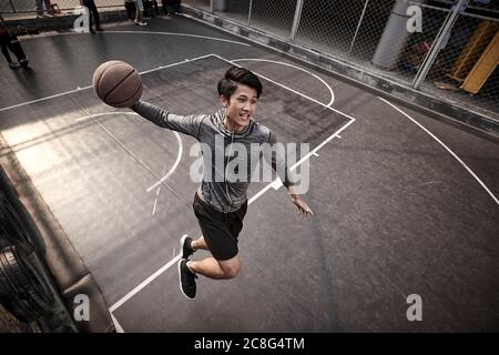 jeune asiatique adulte homme joueur de basket-ball essayant une dunk slam sur le terrain extérieur Banque D'Images