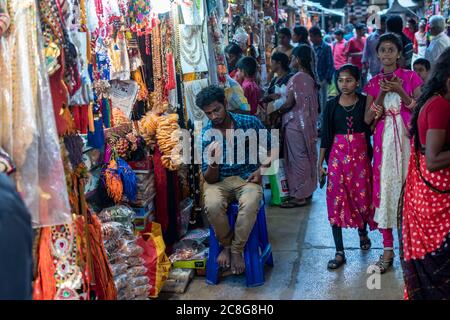 Trichy, Tamil Nadu, Inde - février 2020 : un jeune commerçant indien vendant des objets d'artisanat et des bijoux assis soigneusement à l'extérieur de son magasin. Banque D'Images