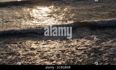 Paysage marin d'été, vagues de mousse se précipitant vers le rivage, les rayons lumineux du soleil couchant se réfléchissent sur la surface de la mer. Vue rapprochée de la falaise. Banque D'Images