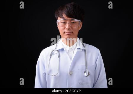 Jeune homme asiatique beau médecin portant des lunettes de protection contre fond noir Banque D'Images