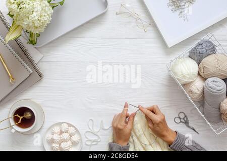 Femmes tricotage de mains avec de la laine blanche, sur un fond en bois, vue de dessus. Accessoires d'artisanat, thé, journal et fleurs d'hortensia. Banque D'Images