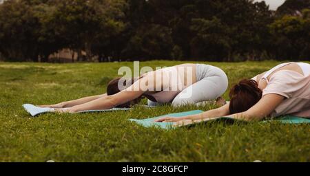 Deux femmes de fitness faisant du yoga dans un parc. Les femmes pratiquant la pose d'enfant tout en faisant du yoga dans le parc. Banque D'Images