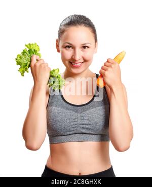 une jeune femme mince, avec une belle figure, tient des légumes dans ses mains - carottes et laitue. Isolé sur fond blanc. Banque D'Images