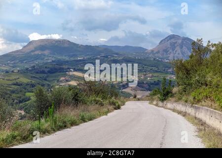 Descente sur une route pavée, avec champs de ferme et montagnes en arrière-plan, Banque D'Images