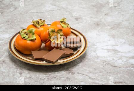 une petite assiette de pésimmons mûrs avec des carrés de chocolat sur un comptoir en marbre gris avec un espace de copie Banque D'Images