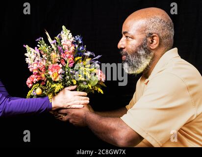 Bouquet de fleurs colorées donné à un mâle afro-américain sur fond noir. Diversité, Fête des mères, Amour ou concept de la Saint-Valentin Banque D'Images