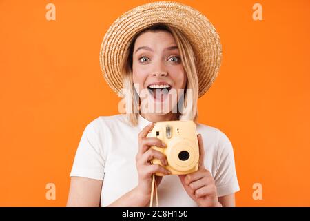 Portrait de jeune femme blonde charmante et gaie portant des vêtements décontractés, isolés sur fond orange, tenant un appareil photo instantané Banque D'Images