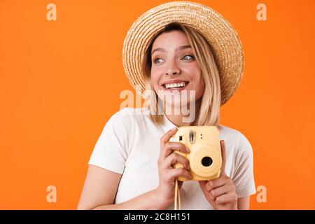 Portrait de jeune femme blonde charmante et gaie portant des vêtements décontractés, isolés sur fond orange, tenant un appareil photo instantané Banque D'Images