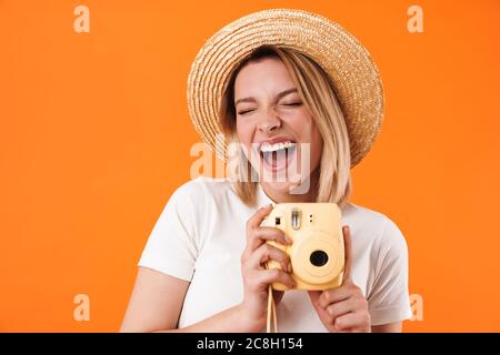 Portrait de jeune femme blonde charmante et gaie portant des vêtements décontractés, isolés sur fond orange, tenant un appareil photo instantané Banque D'Images