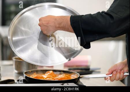Gros plan, chef recouvrant la poêle avec couvercle dans la cuisine du restaurant. Photo de haute qualité. Banque D'Images