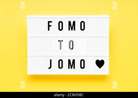 FOMO À JOMO écrit en boîte lumineuse sur fond jaune. Choix, concept de problème social. Vue de dessus, espace de copie Banque D'Images