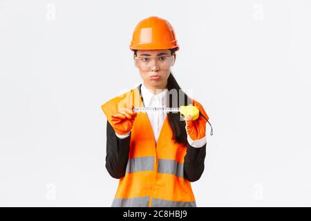 Déçue femme asiatique ingénieur de construction, architecte montrant petite taille sur mètre ruban, en poudant contrarié avec des mesures, debout Banque D'Images