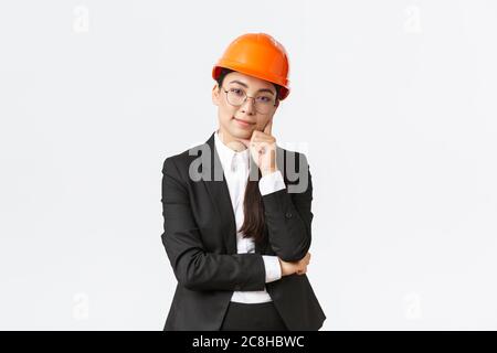 Une femme d'affaires asiatique souriante investit de l'argent dans la construction, gère le travail en entreprise, porte un casque de sécurité et un costume, et regarde avec plaisir Banque D'Images