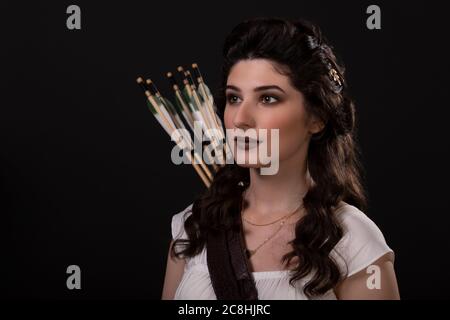 Portrait en gros plan d'une femme archer en robe blanche sur fond noir. La déesse grecque Artemis. Prise de vue en studio. Maquillage professionnel et coiffure f Banque D'Images