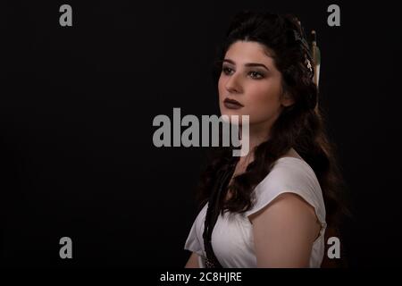 Portrait en gros plan d'une femme archer en robe blanche sur fond noir. La déesse grecque Artemis. Prise de vue en studio. Maquillage professionnel et coiffure f Banque D'Images