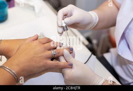 L'huile de manucure naturelle s'écoule de la pipette sur les doigts du client des mains de la femme. Soins des ongles après la quarantaine. Travail d'un manucure dans le salon. Mains de Banque D'Images