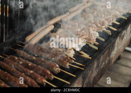 Vue rapprochée sur le gril de viande de poulet, Kebabs et saucisses sur le long barbecue rectangulaire avec fumée à l'extérieur de la rue. Barbecue d'été. BB Banque D'Images