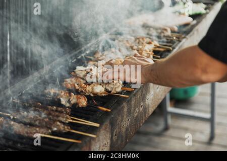 Main de jeune homme de griller de la viande et des légumes sur un long barbecue rectangulaire avec de la fumée sur la rue à l'extérieur. Barbecue d'été. Barbecue avec Banque D'Images