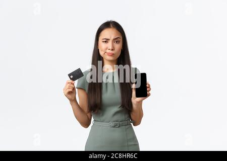 Propriétaires de petites entreprises, femmes entrepreneurs concept. Femme asiatique sceptique et suspecte tenant une carte de crédit, montrant l'écran de téléphone mobile avec Banque D'Images