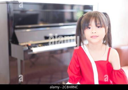 Un portrait d'une adorable fille d'école élémentaire asiatique portant une chemise rouge assise dans la salle d'entraînement du piano Banque D'Images