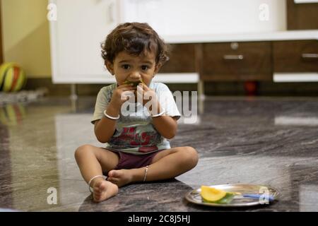 Un petit garçon est assis sur une pierre de marbre mangeant des mangues et gardant des mangues hachées dans une palette près de l'enfant. Banque D'Images