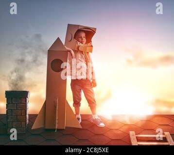 Un petit garçon joue à l'astronaute. Enfant sur fond de ciel de coucher de soleil. Enfant dans un costume d'astronaute debout sur le toit de la maison et looki Banque D'Images