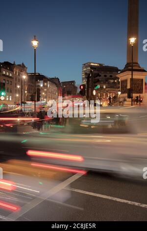 Impression de vitesse et de circulation rapide vue contre les piétons sur un passage à niveau près de la colonne Nelson de Trafalgar Square à Londres après la tombée de la nuit. Banque D'Images