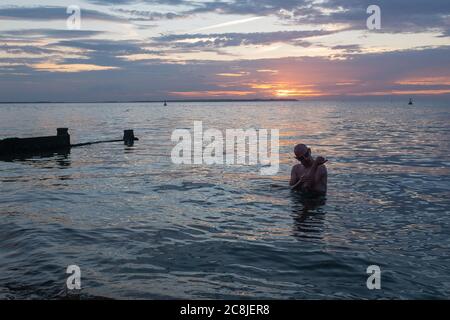 Alors que le soleil se couche sur la lumière du jour et les eaux calmes de l'estuaire de la Tamise, un nageur de mer sauvage sort soigneusement de l'eau après son plongeon régulier en soirée, le 18 juillet 2020, à Whitstable, Kent, Angleterre. Banque D'Images