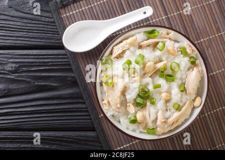 Gros plan sur le porridge de riz au gingembre cuit lentement avec du poulet, des arachides et des oignons verts dans un bol sur la table. Vue horizontale du dessus Banque D'Images