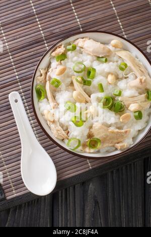 Bouillie de riz au poulet bouilli, aux arachides et aux oignons verts dans un bol sur la table. Vue verticale du dessus Banque D'Images