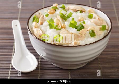 Faites un tour de bouillie de riz légèrement salée avec du poulet, des arachides et des oignons verts dans un bol sur la table. Horizontal Banque D'Images