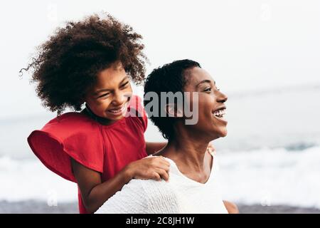 Mère noire et fille courant sur la plage au coucher du soleil pendant les vacances d'été - les gens de famille s'amusant ensemble en plein air - Voyage et happines