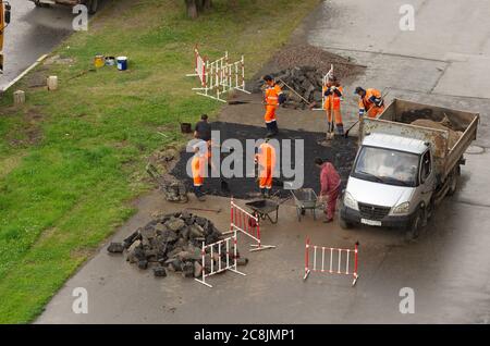 Saint-Pétersbourg, Russie - 28 juillet 2019 : une équipe de travailleurs en combinaisons orange dépose de l'asphalte sur le trottoir par temps pluvieux Banque D'Images