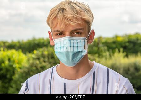 Garçon adolescent garçon jeune homme portant un masque facial à l'extérieur pendant la pandémie du coronavirus COVID-19 Banque D'Images