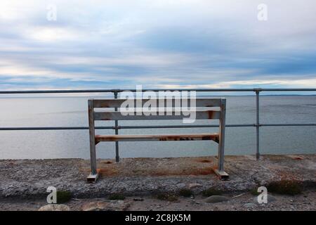 Banc en métal rouillé, avec vue sur les barrières métalliques de la mer d'Irlande au coucher du soleil à Trefor, au nord du pays de Galles Banque D'Images